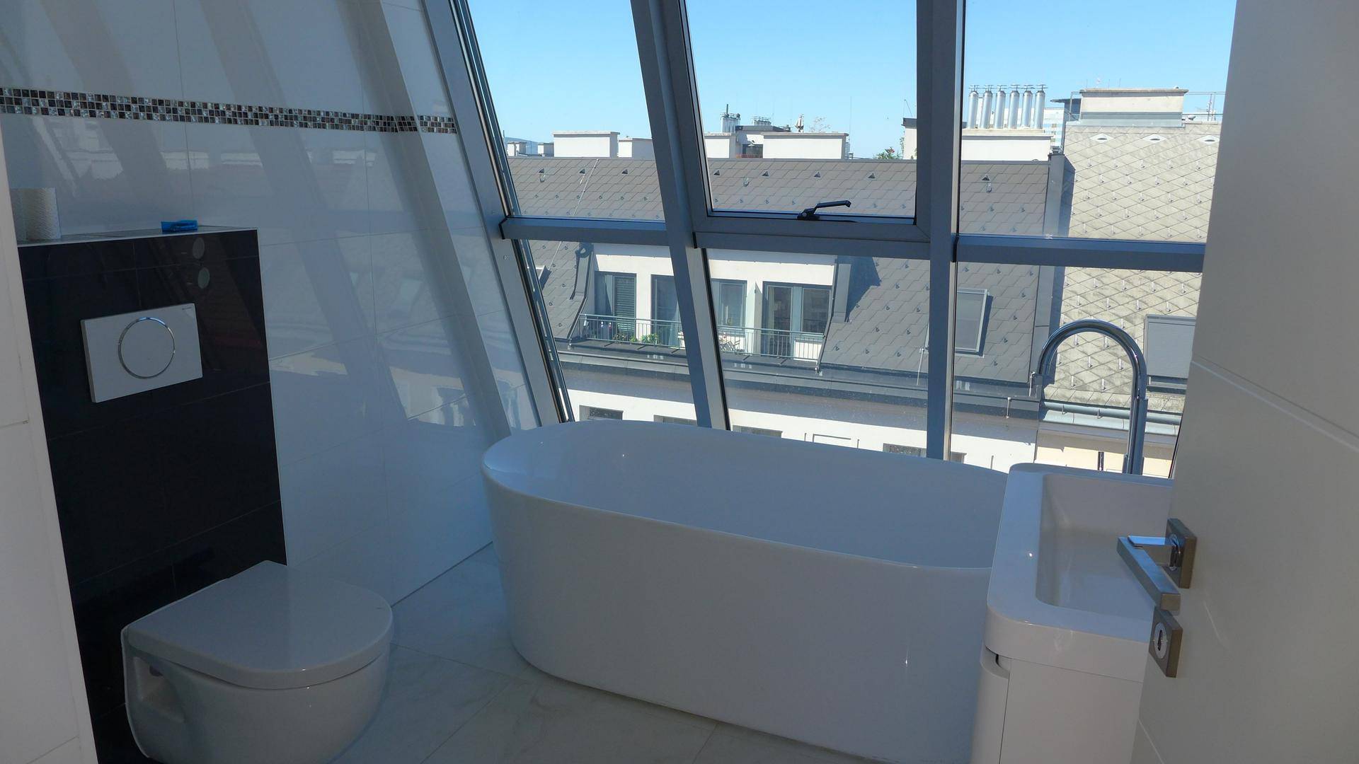 Modernes Badezimmer mit freistehender Badewanne, wandhängendem WC und großem Fenster mit Stadtblick.