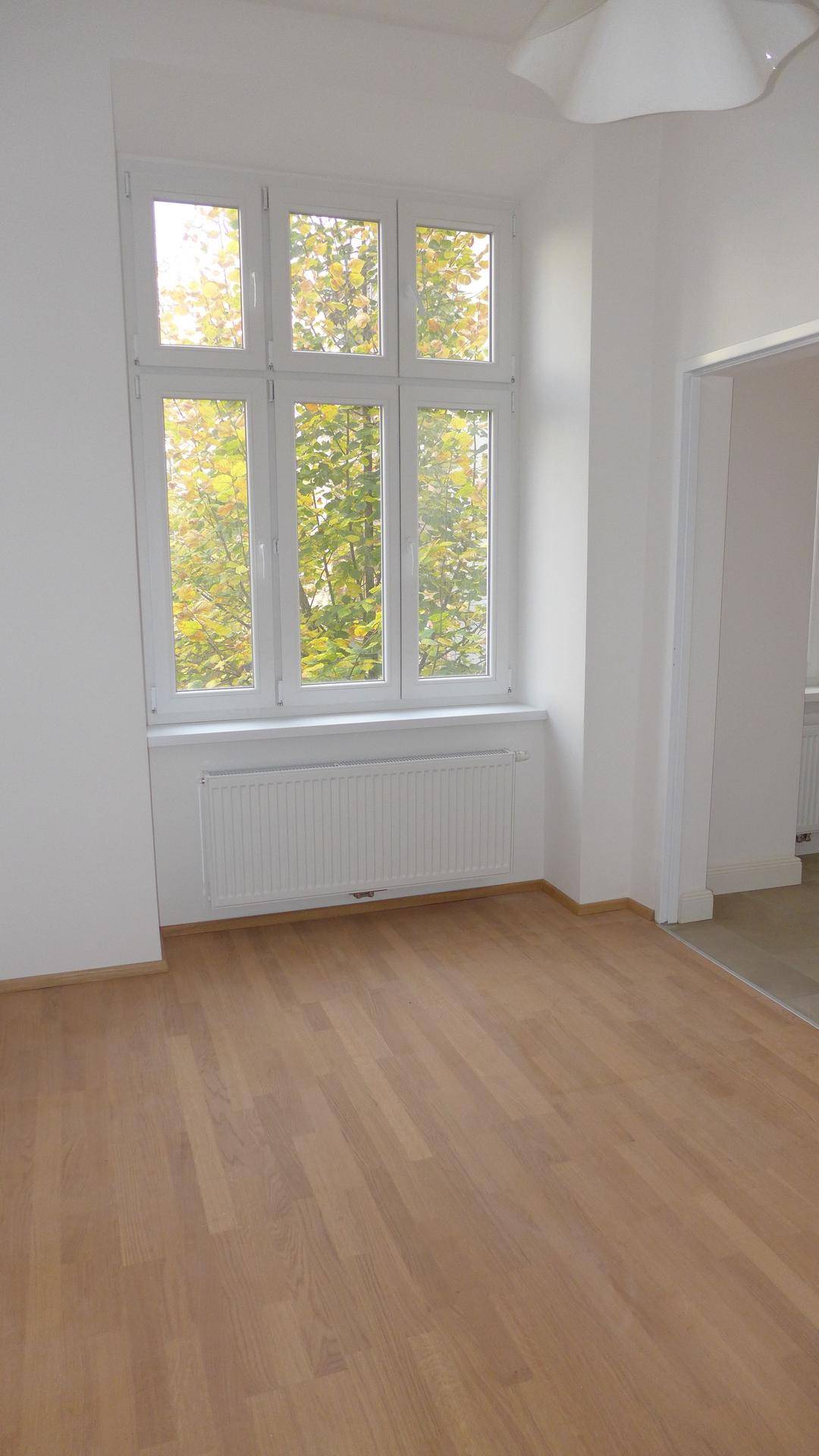 Helles Zimmer mit Parkettboden und einem großen Fenster, das einen schönen Blick ins Grüne bietet.