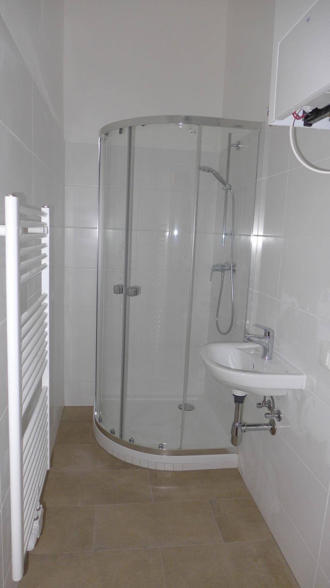 Modernes Badezimmer mit Duschkabine, Waschbecken und beheiztem Handtuchhalter in hellen Farbtönen.