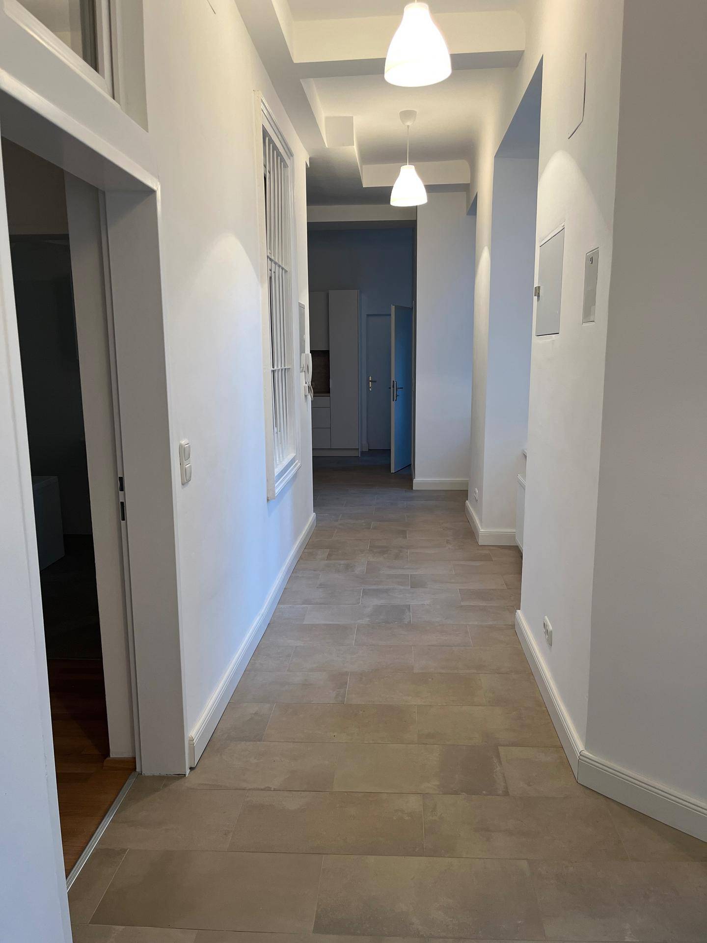 Heller Flur mit modernen Hängelampen und beigefarbenen Fliesen, der zu weiteren Räumen führt.