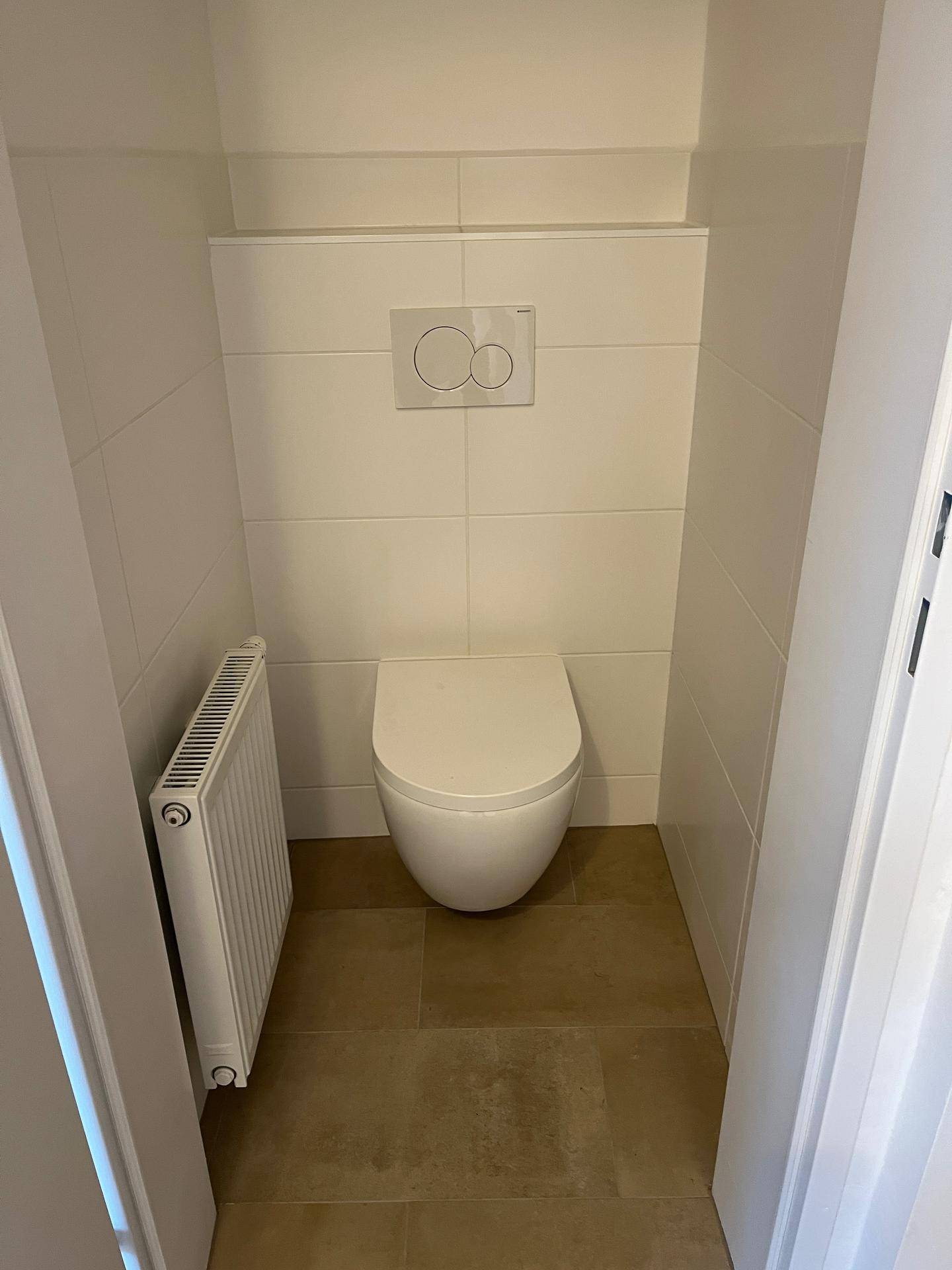 Kompaktes Gäste-WC mit wandhängender Toilette, weißen Fliesen und Heizkörper.