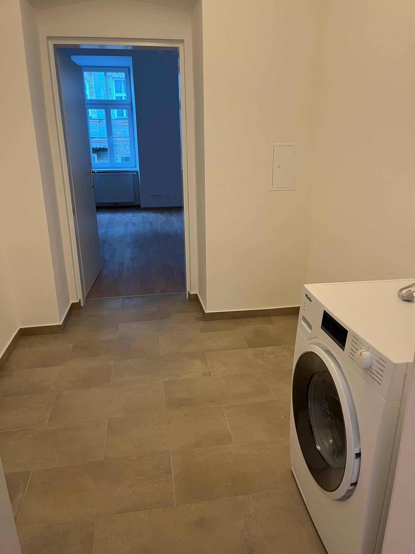 Praktischer Hauswirtschaftsraum mit Waschmaschine und Fliesenboden, angrenzend an ein weiteres Zimmer.