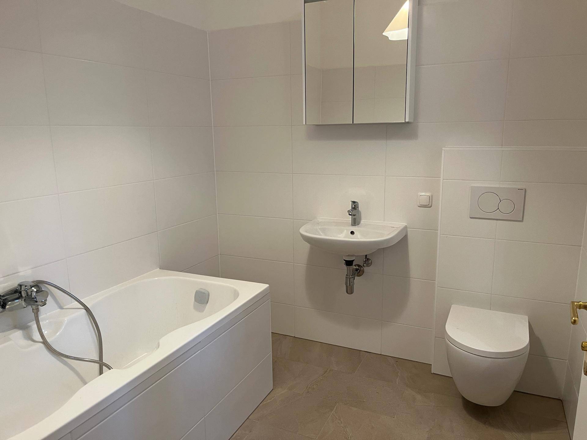Geräumiges Badezimmer mit Badewanne, Waschbecken, wandhängender Toilette und Spiegelschrank.