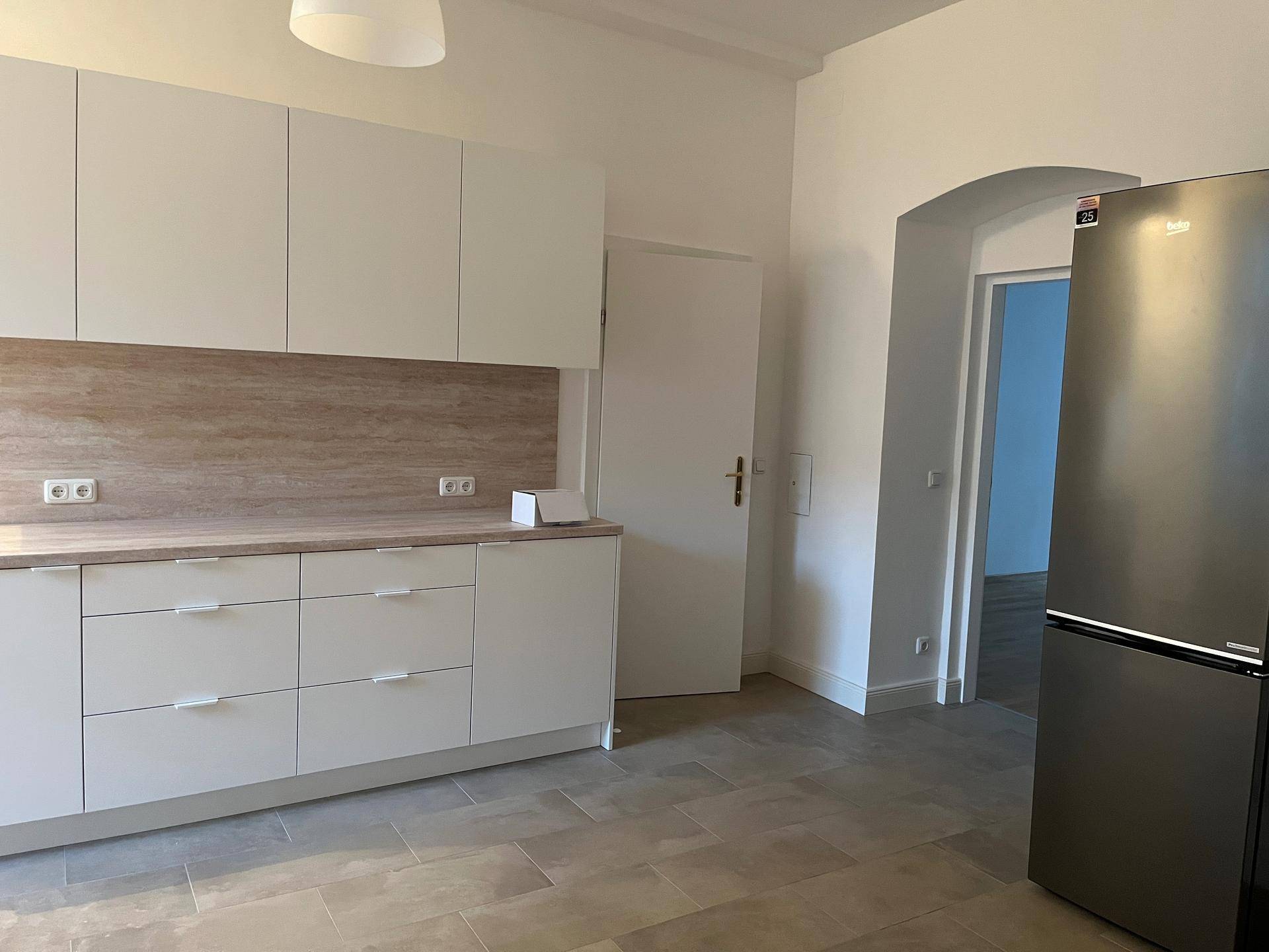 Funktionale Küche mit weißen Unterschränken, Arbeitsplatte in Holzoptik und einem freistehenden Kühlschrank.