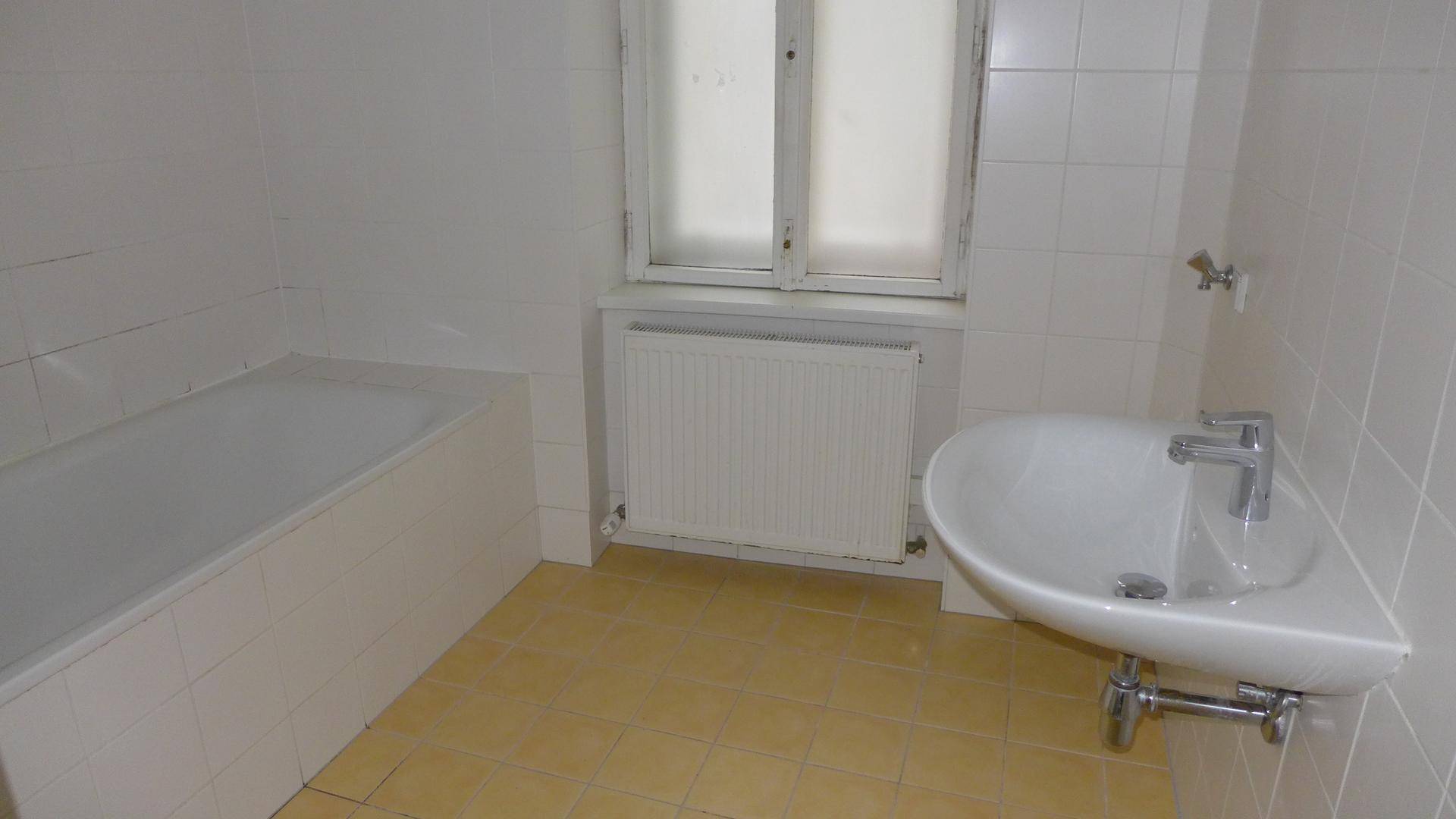 Badezimmer mit Badewanne, Waschbecken und Fenster, gefliest in Weiß und Gelb.