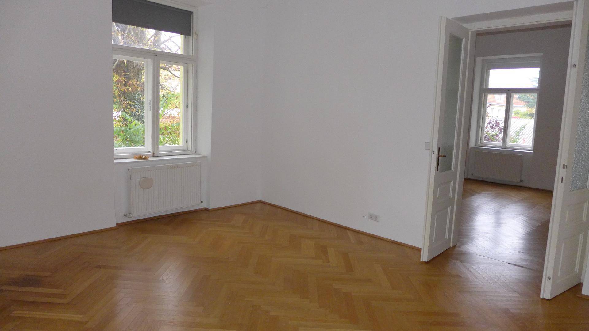 Wohnzimmer mit Fischgrätparkettboden und Blick durch die Fenster auf die umliegende Natur.