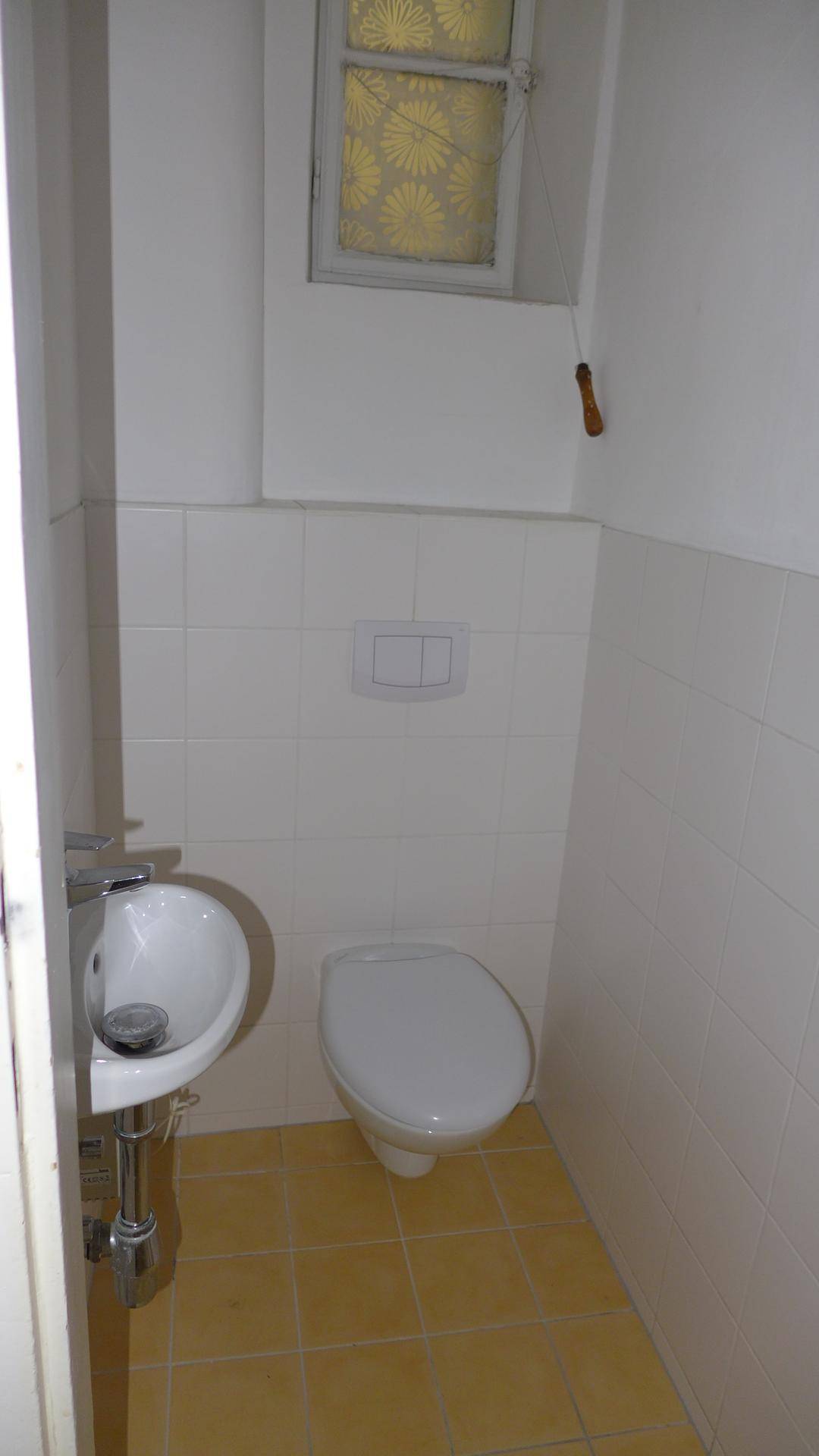 Separate Gästetoilette mit WC, kleinem Waschbecken und Fenster für natürliche Belüftung.