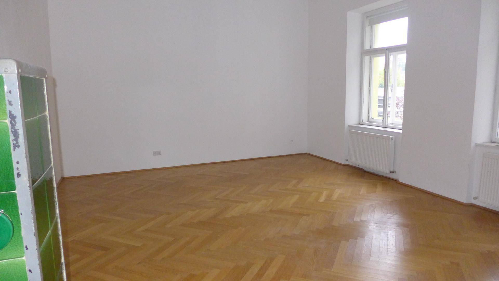 Helles Wohnzimmer mit Fischgrätparkettboden, weiß gestrichenen Wänden und großen Fenstern.