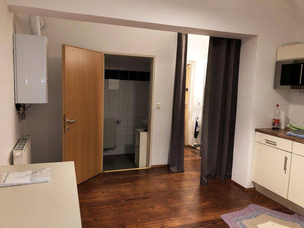 Kleine Küchenzeile mit Boiler und Heizkörper, dunklem Holzboden und Zugang zu einem gefliesten Bad.