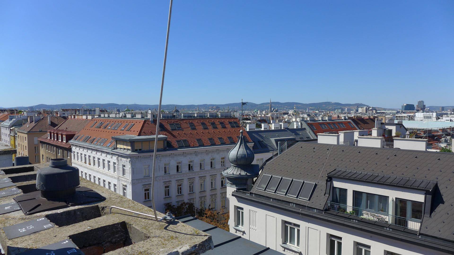 Panoramablick über die Dächer der Stadt mit Bergen am Horizont unter blauem Himmel.
