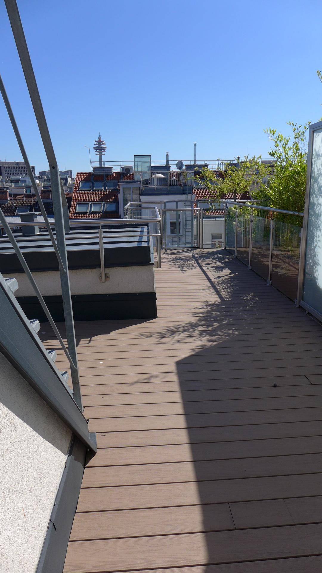 Dachterrasse mit Holzboden und Blick auf die umliegenden Gebäude und den Himmel.