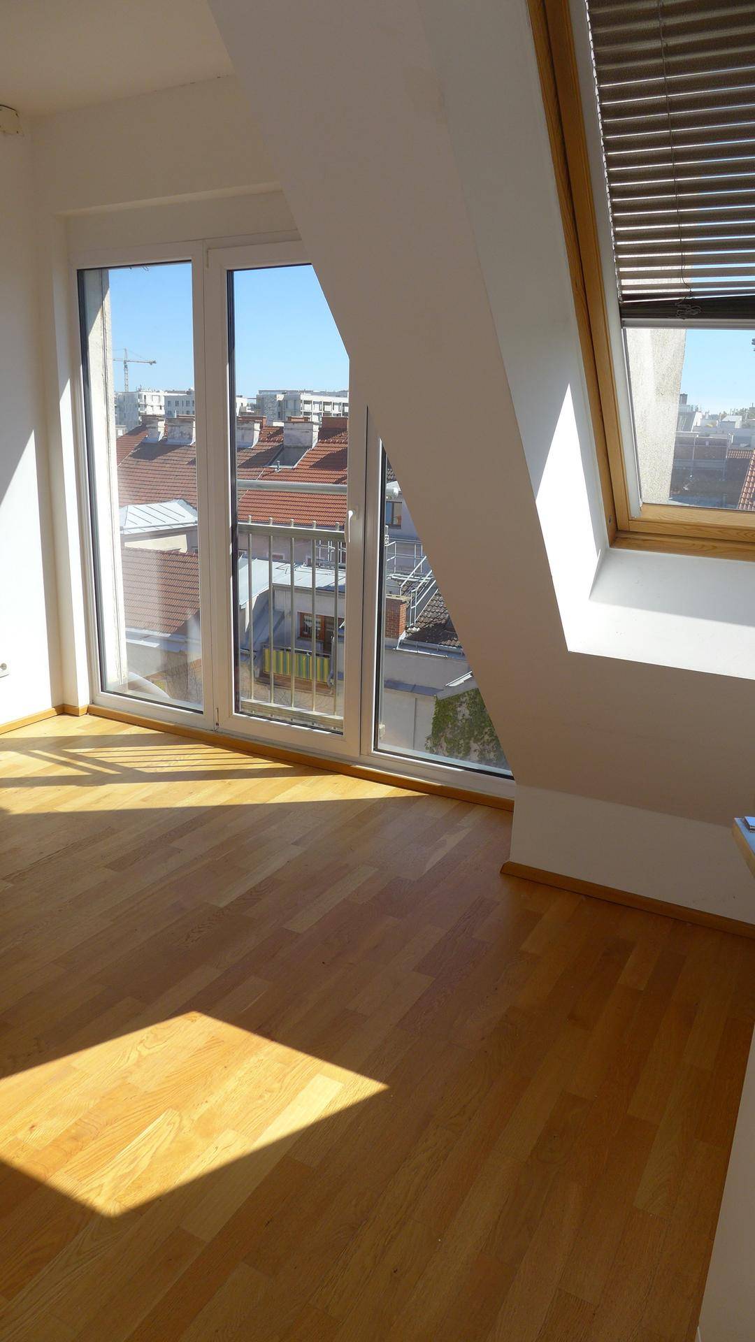 Heller Raum mit Holzparkettboden und großen Fenstern, die Zugang zu einem Balkon bieten.