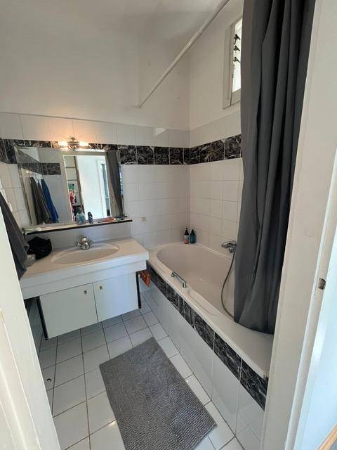 Badezimmer mit Badewanne, Waschbecken und weißen Fliesen, ausgestattet mit einem Fenster.