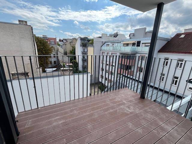 Geräumiger Balkon mit Holzfußboden und Metallgeländer, bietet Blick auf die städtische Umgebung.