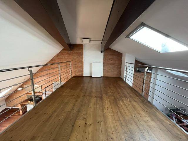 Offene Galerie mit Holzboden, Ziegelwänden und Blick auf den darunterliegenden Wohnbereich.