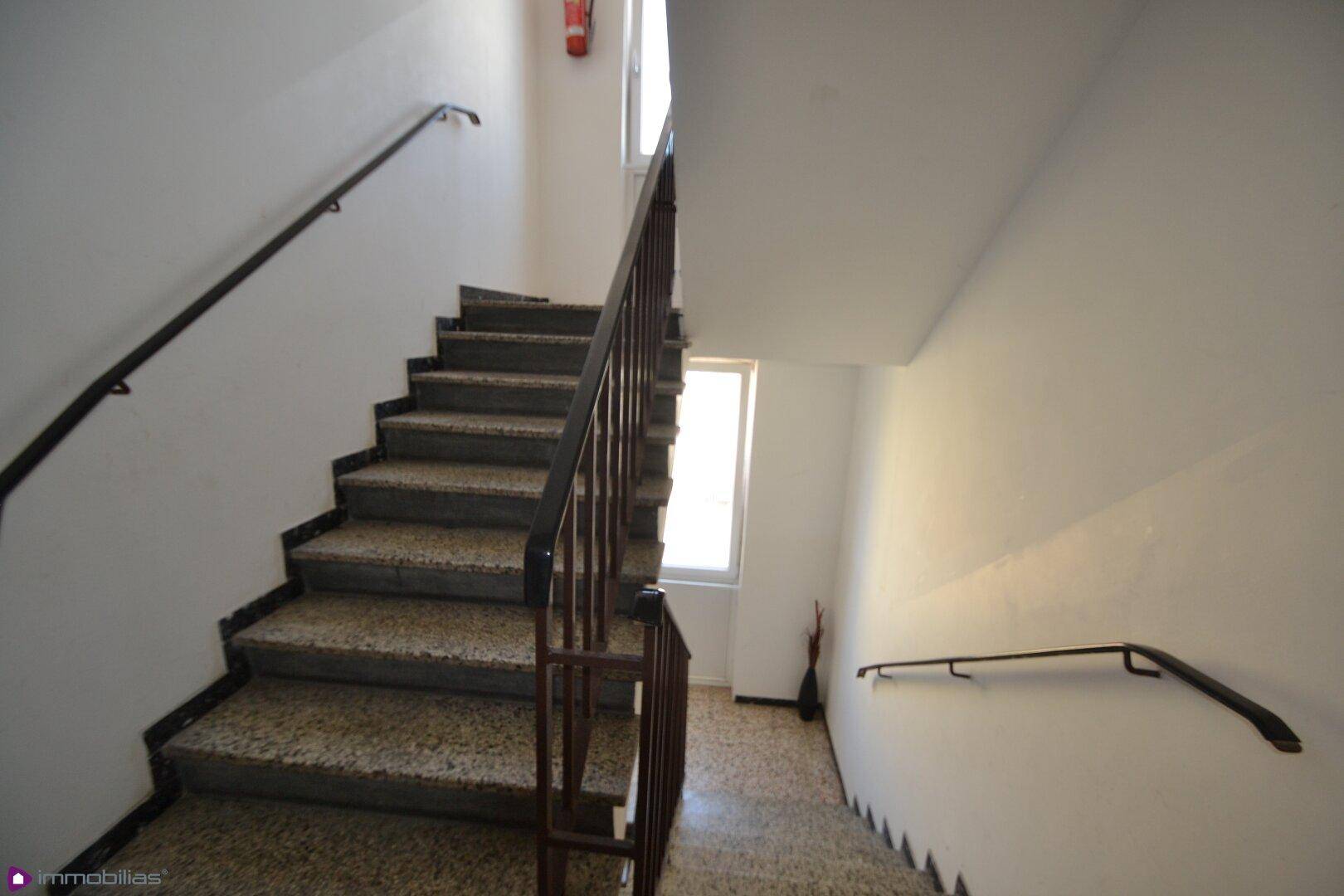 Treppenhaus mit Steinstufen und Handläufen, gut beleuchtet durch ein Fenster.