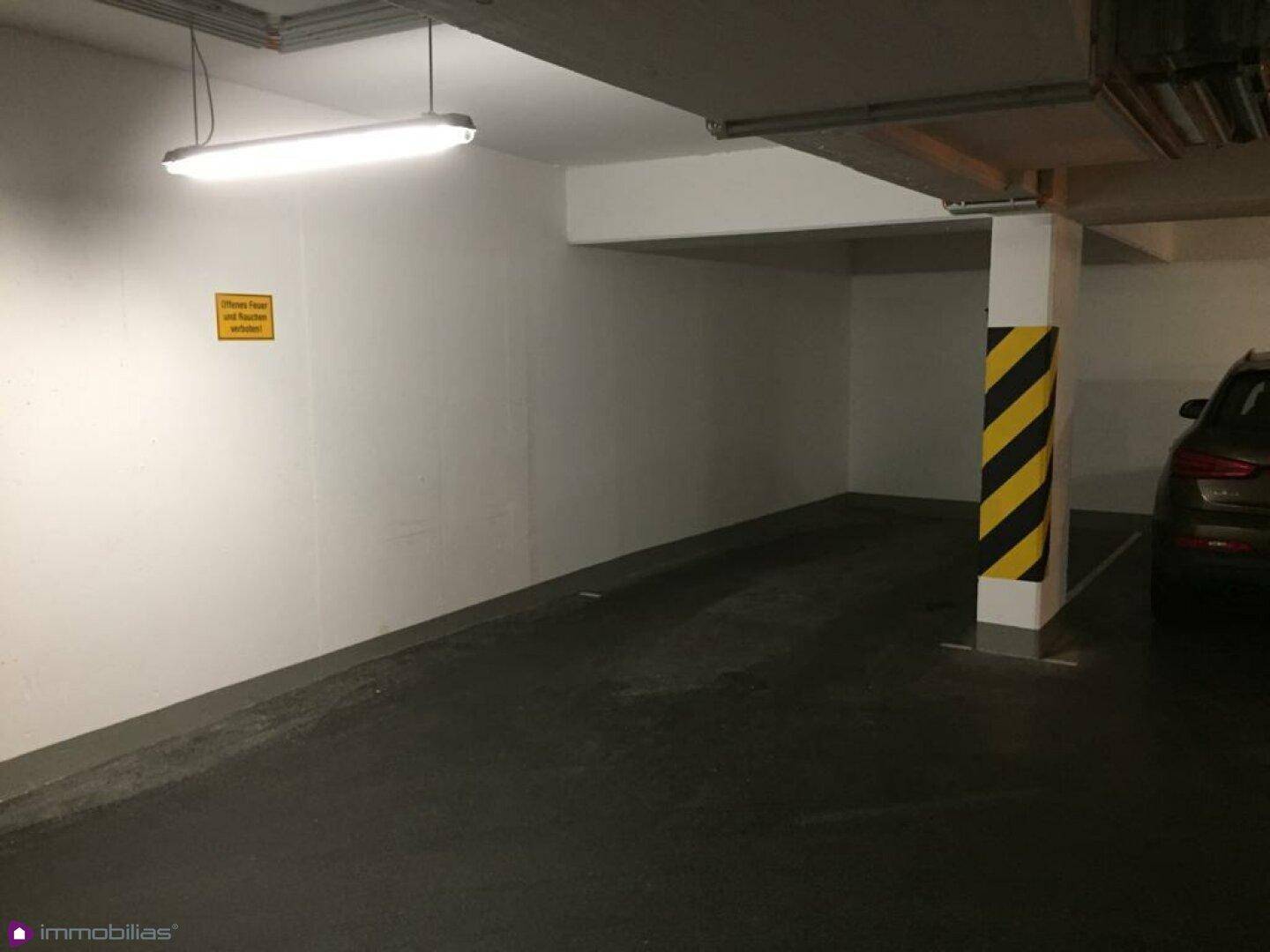 Leerer Stellplatz in einer Tiefgarage mit gelb-schwarz markierter Säule und Beleuchtung.