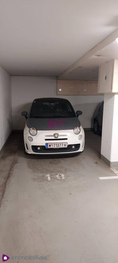 Ein kleines Auto parkt auf einem markierten Stellplatz in einer hellen Tiefgarage.