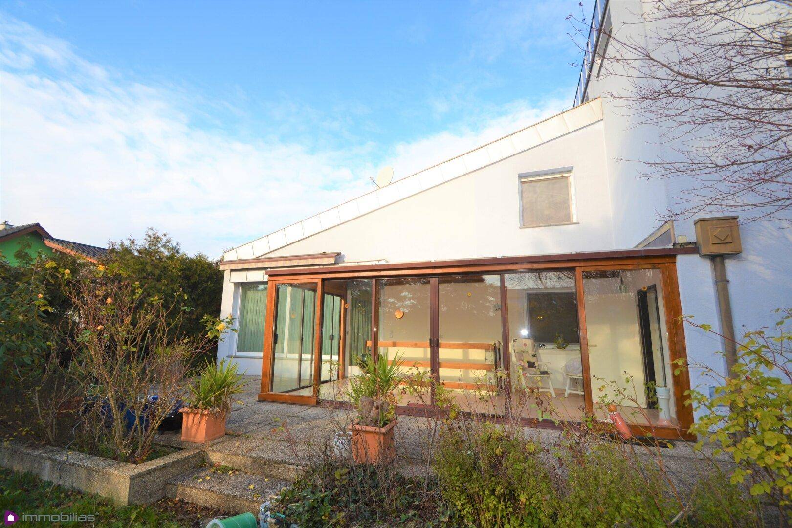 Rückansicht des Hauses mit großem Wintergarten und Gartenbereich unter blauem Himmel.