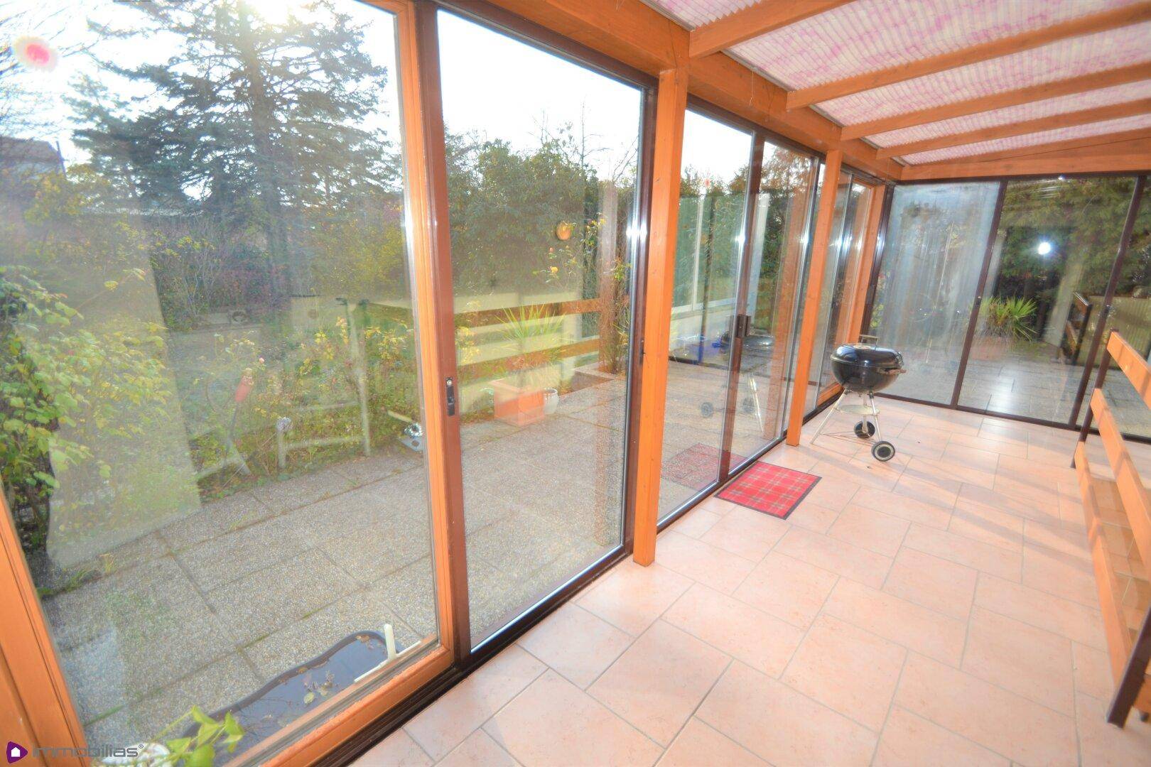 Heller Wintergarten mit Fliesenboden, großen Glasfronten und Zugang zum Außenbereich.