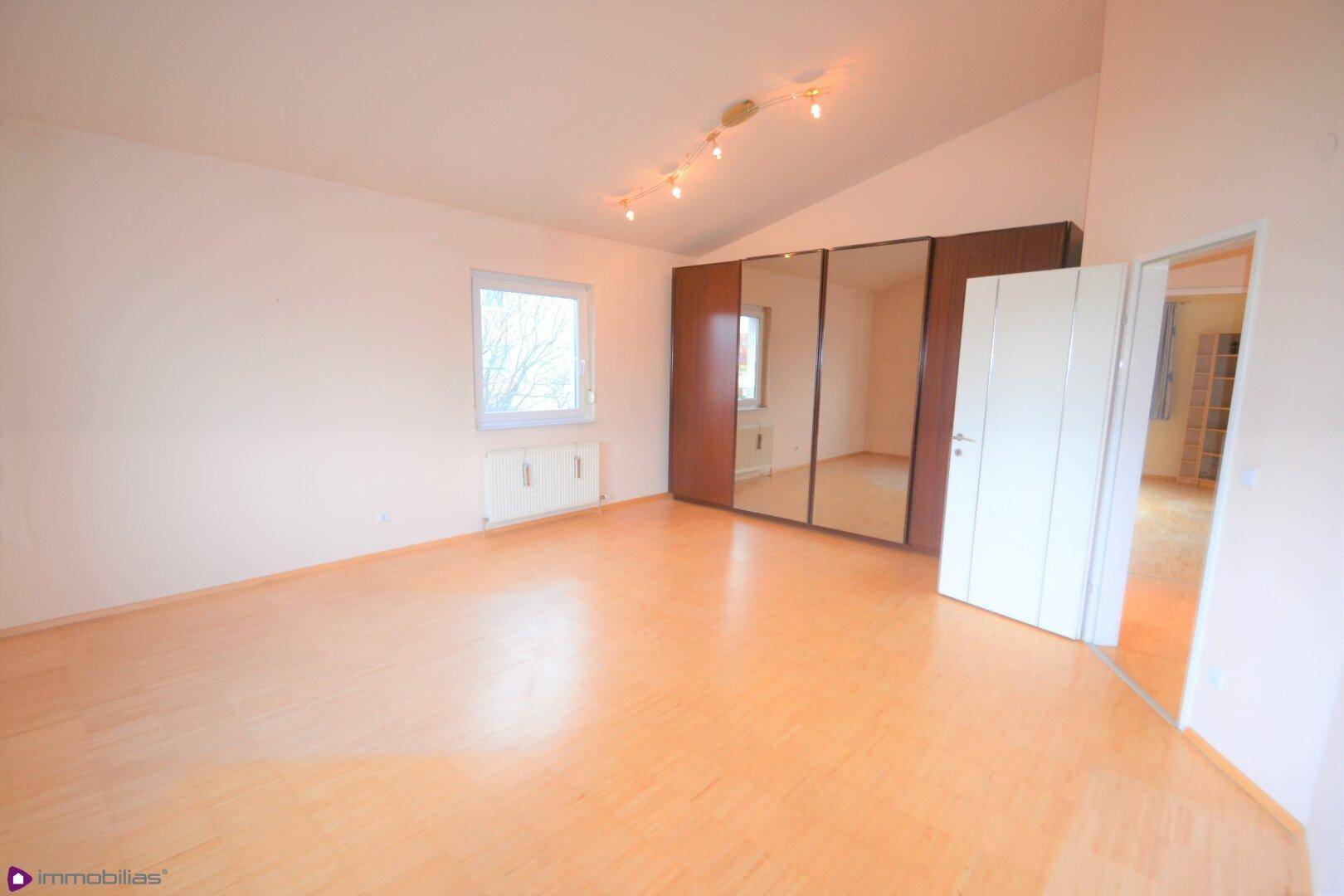 Schlafzimmer mit Parkettboden, Dachschräge und einem großen Spiegelschrank.