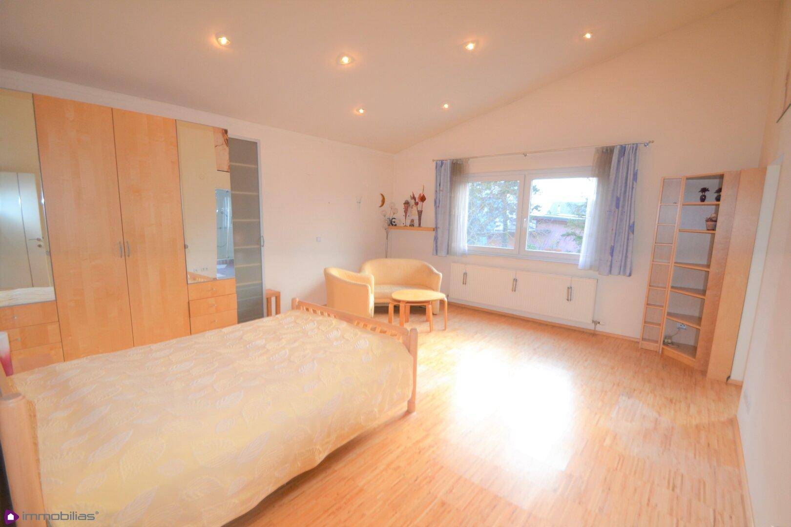Gemütliches Schlafzimmer mit Parkettboden, Dachschräge und viel natürlichem Licht durch das Fenster.