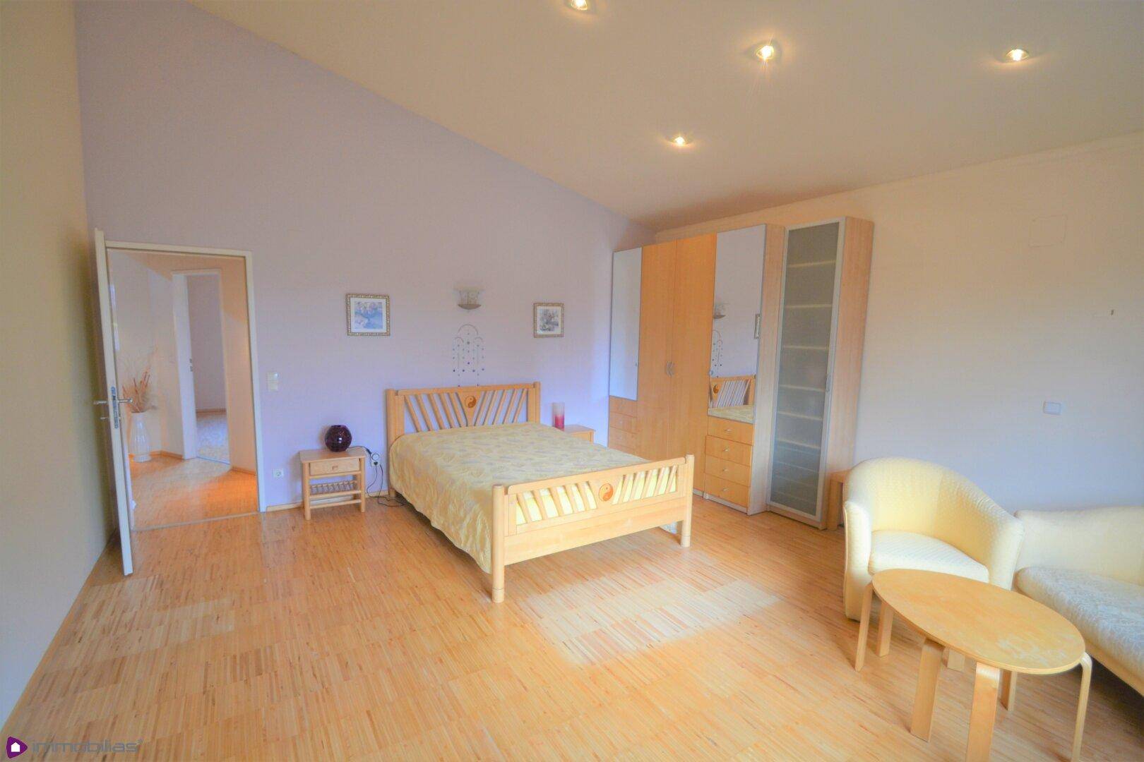 Schlafzimmer mit Holzbett, Parkettboden und Einbauschränken unter einer Dachschräge.