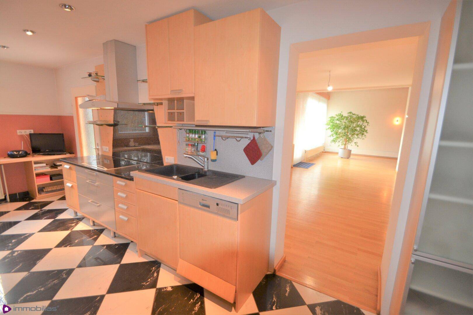 Küche mit hellen Holzfronten, integrierten Geräten und Blick in das angrenzende Wohnzimmer.