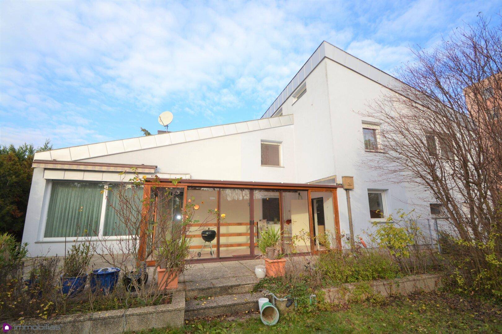 Rückansicht des Hauses mit Wintergarten und Zugang zum Gartenbereich unter blauem Himmel.