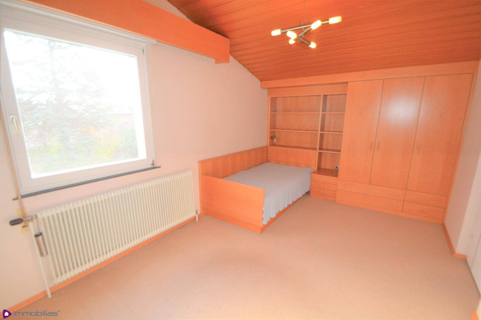 Kinderzimmer mit Holzbett, Einbauschränken und Holzdecke unter einer Dachschräge.
