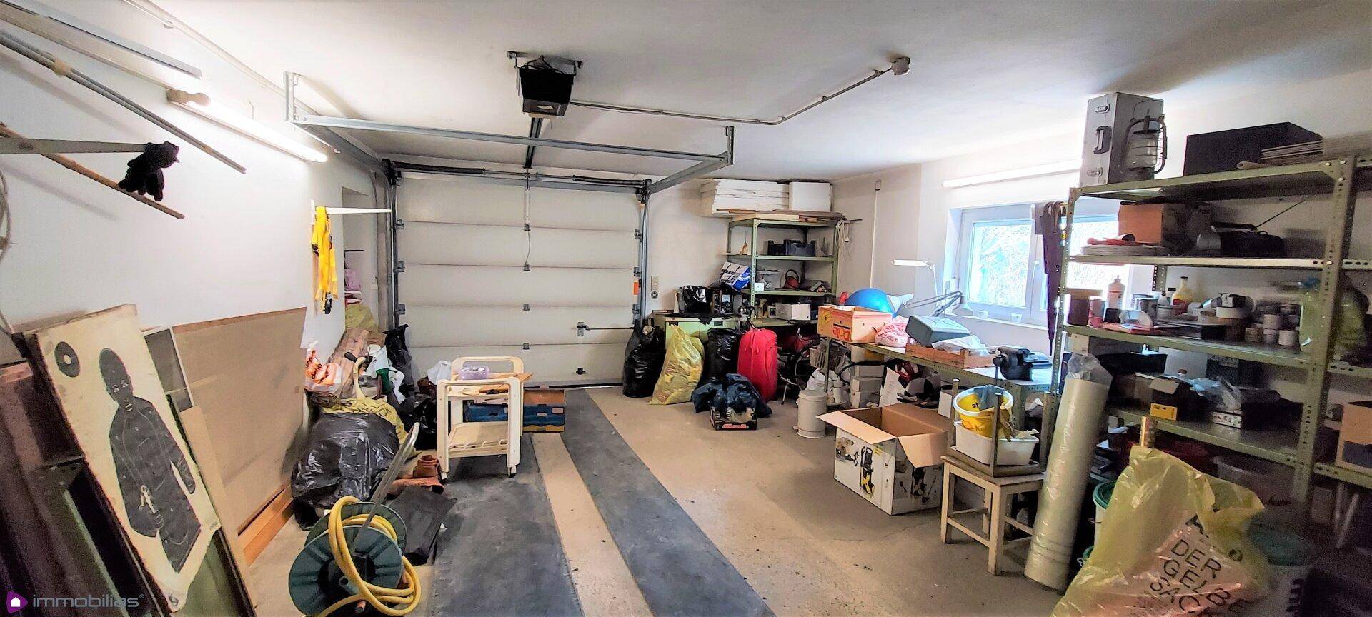 Geräumige Garage mit Rolltor, Regalen und Fenster, die als Lagerraum genutzt wird.
