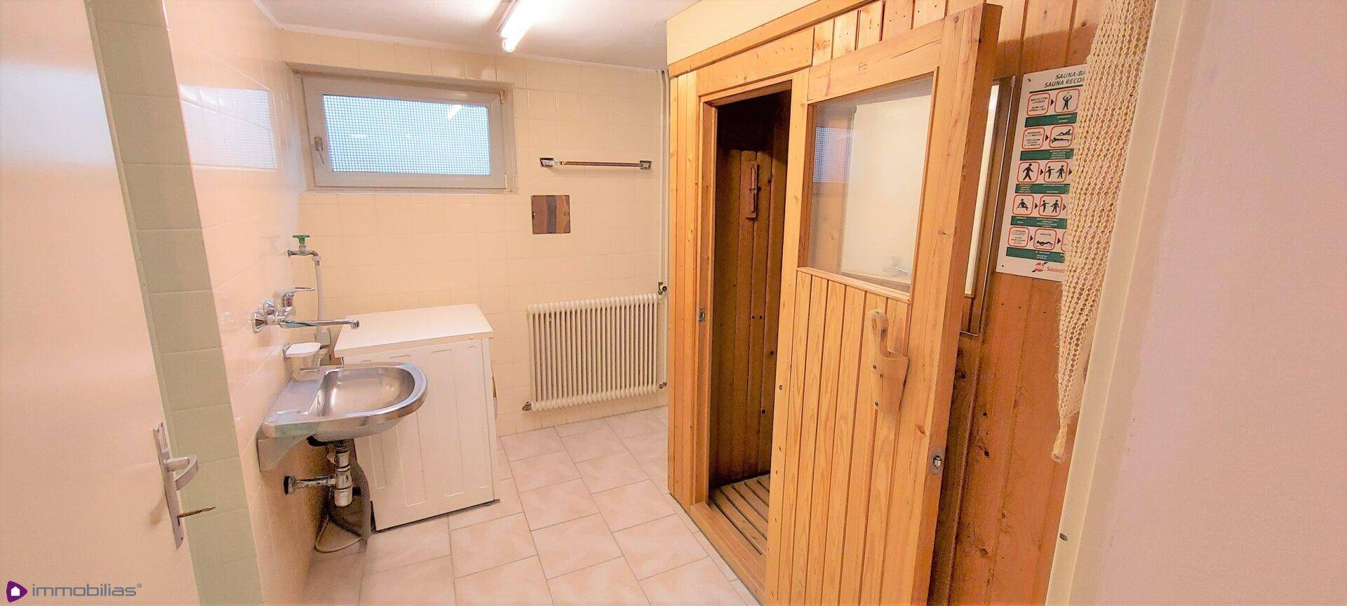 Badezimmer mit Holzsauna, Waschbecken, Heizkörper und Fenster für natürliche Belüftung.