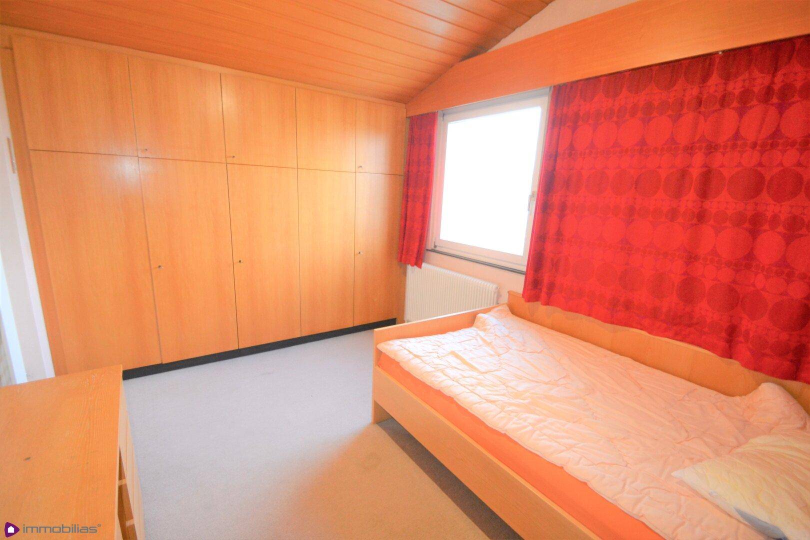Schlafzimmer mit Teppichboden, großen Einbauschränken und Fenster mit roten Vorhängen.
