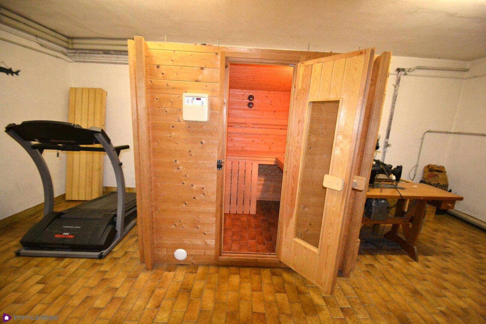 Sauna-Kabine in einem Kellerraum mit Trainingsgerät und Arbeitsbereich.