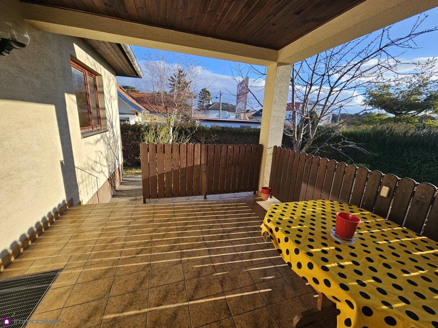 Sonnige überdachte Terrasse mit Fliesenboden und Holzzaun, ideal zum Entspannen.