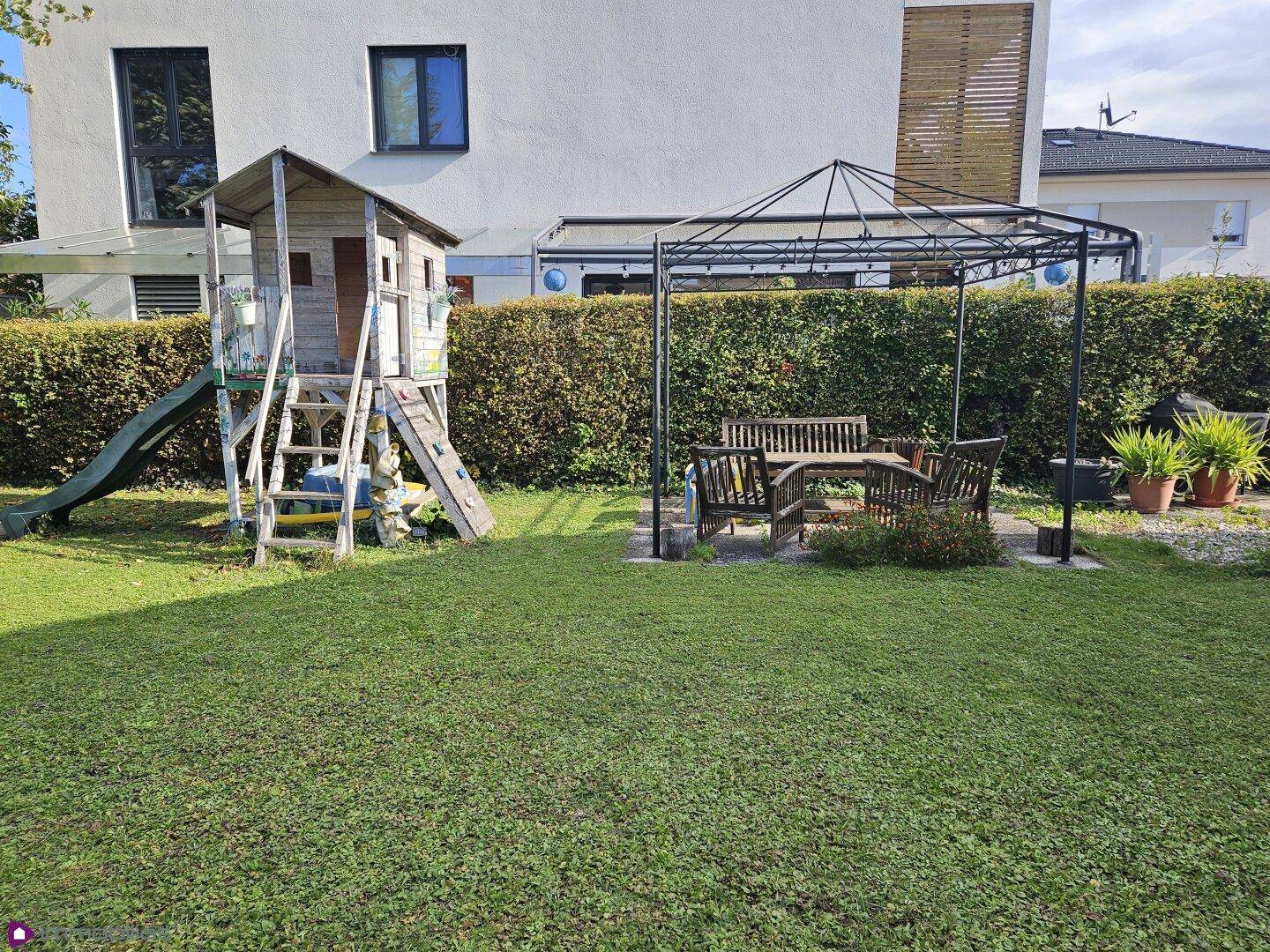 Gepflegter Garten mit Kinderspielhaus und einem Essbereich unter einem Pavillon.