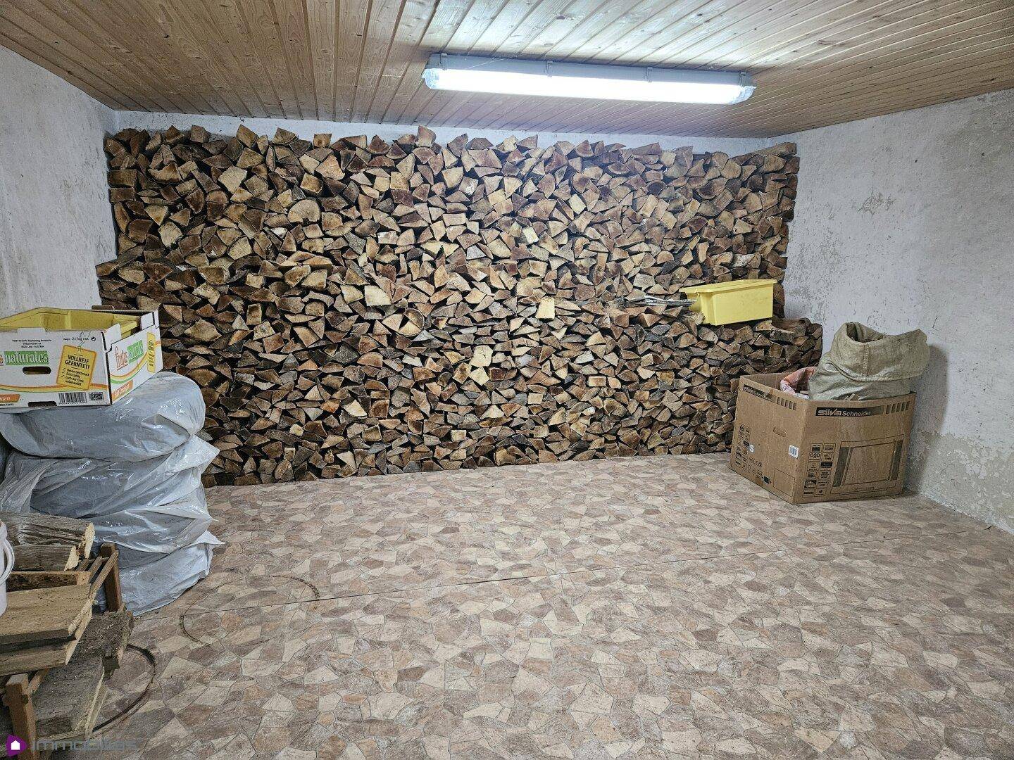 Kellerraum mit gestapeltem Brennholz und einfacher Holzdecke, genutzt als Lagerfläche.