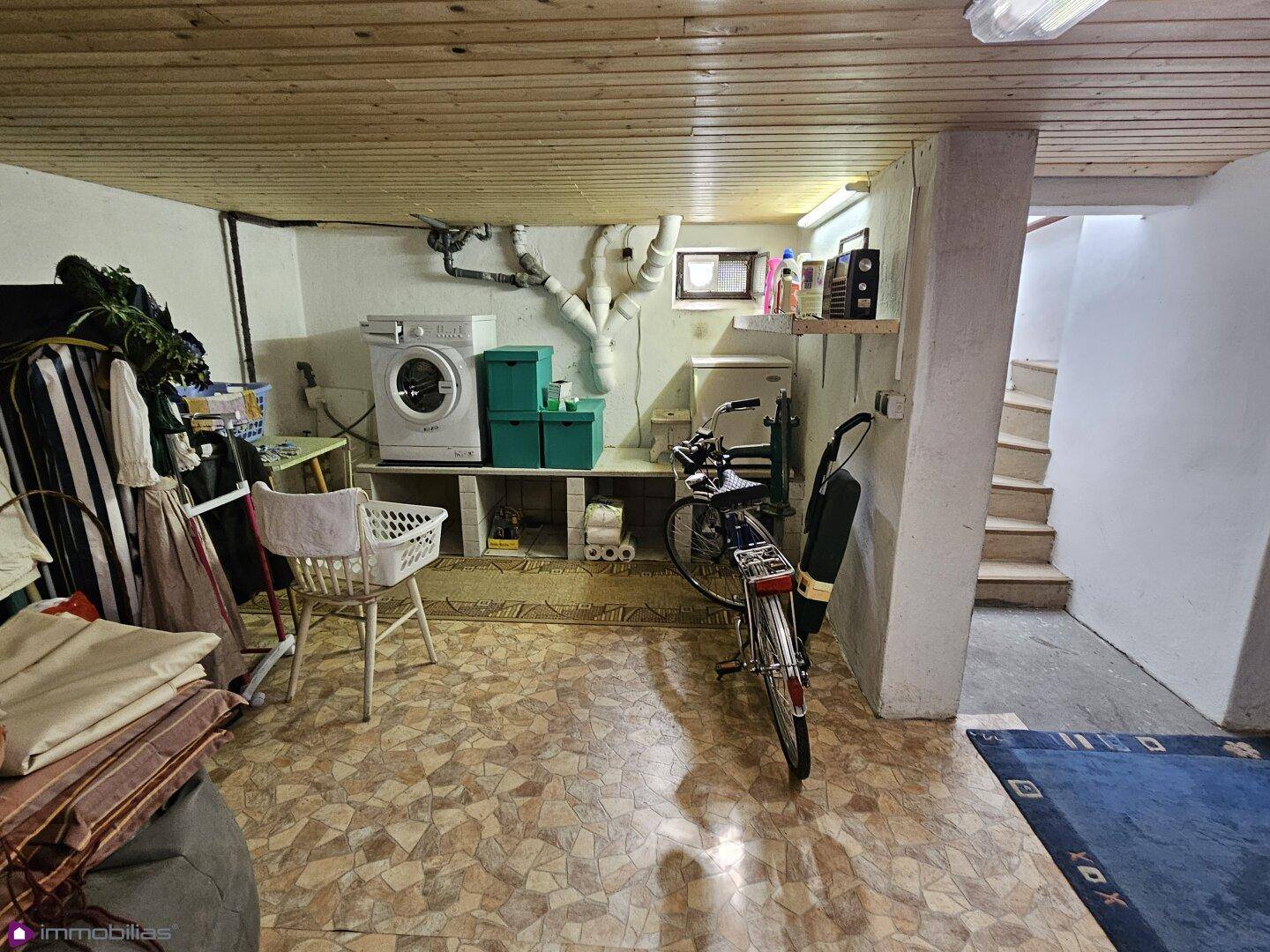 Waschküche im Keller mit Waschmaschine, Trockner und Stauraum, mit Zugang zur Treppe.
