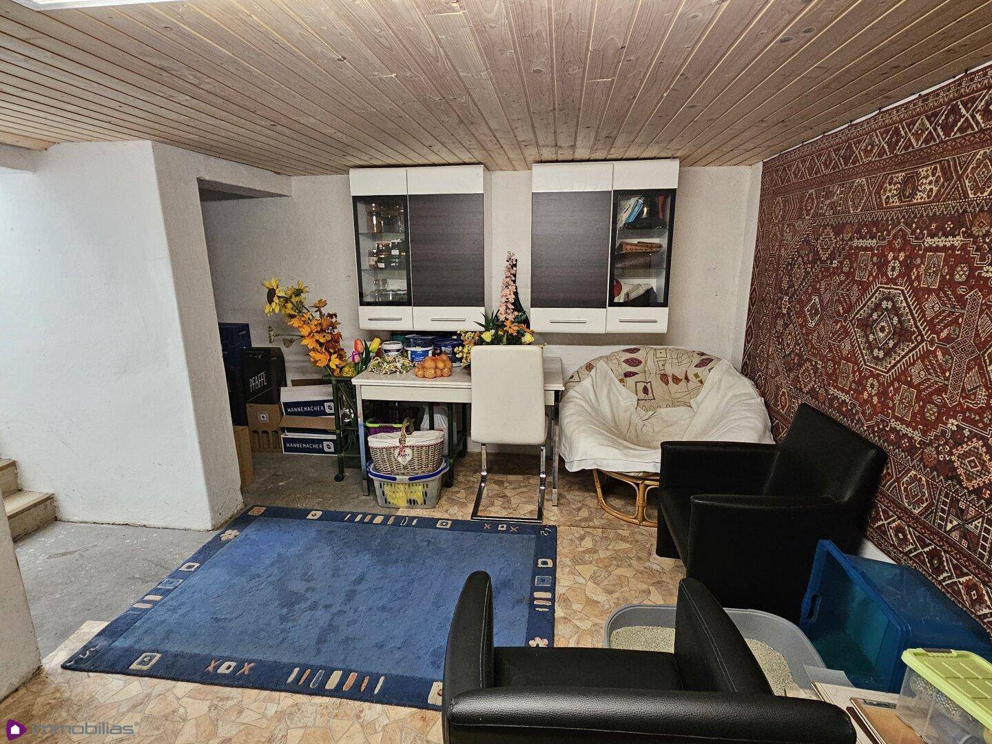 Vielseitig nutzbarer Kellerraum mit Sitzgelegenheiten, Teppich und Holzdecke.
