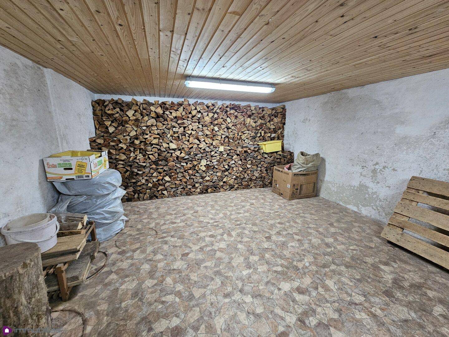 Geräumiger Kellerraum mit Holzdecke und einer Wand aus gestapeltem Brennholz.