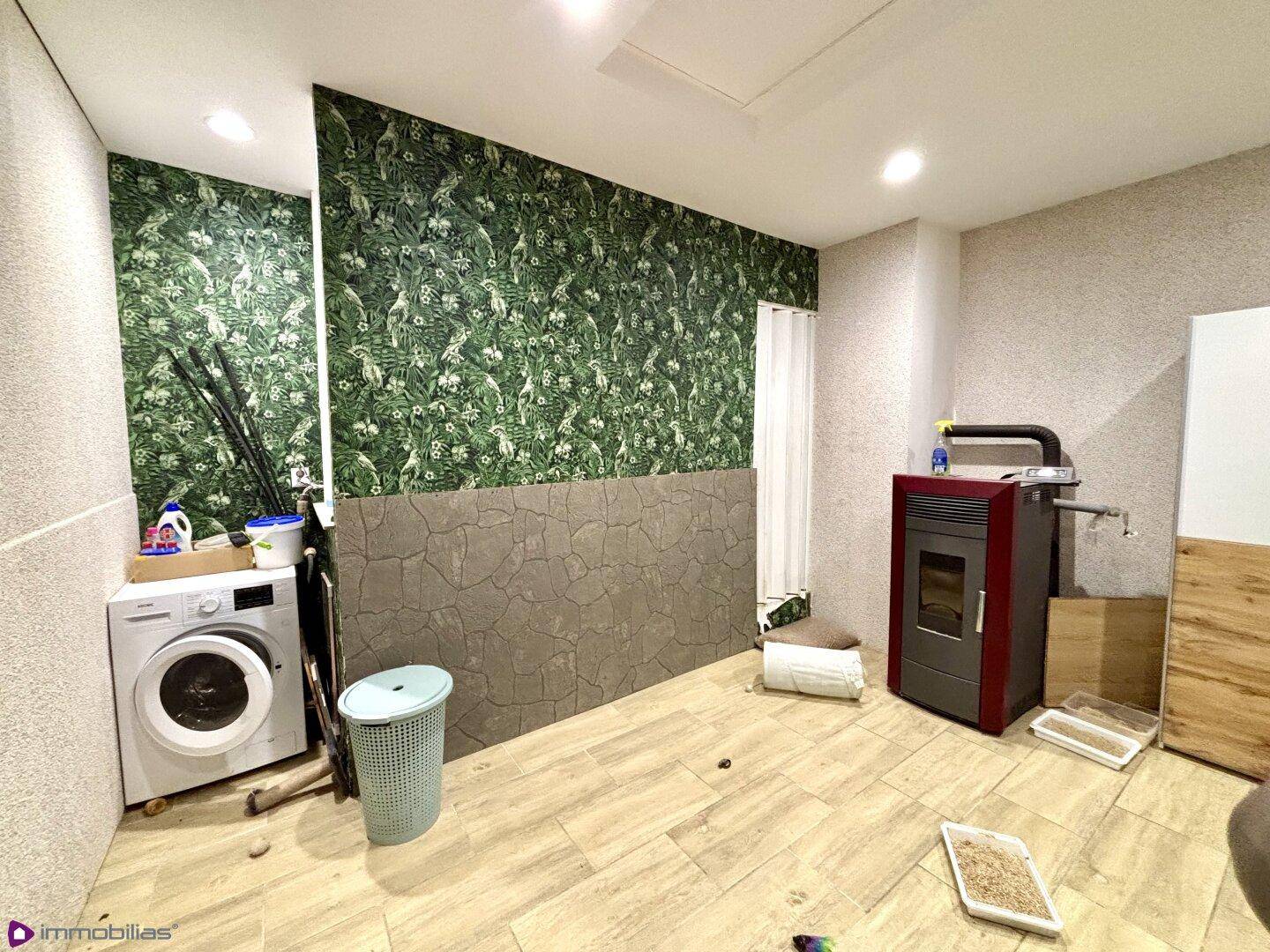 Hauswirtschaftsraum mit Waschmaschine, Pelletofen und grüner Mustertapete.