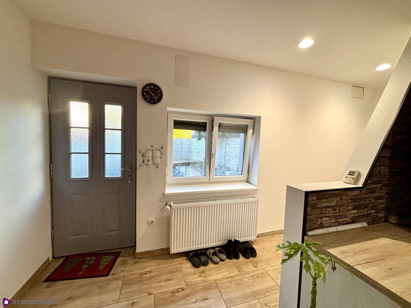 Eingangsbereich mit grauer Haustür, Fenster, Heizkörper und Fliesenboden.