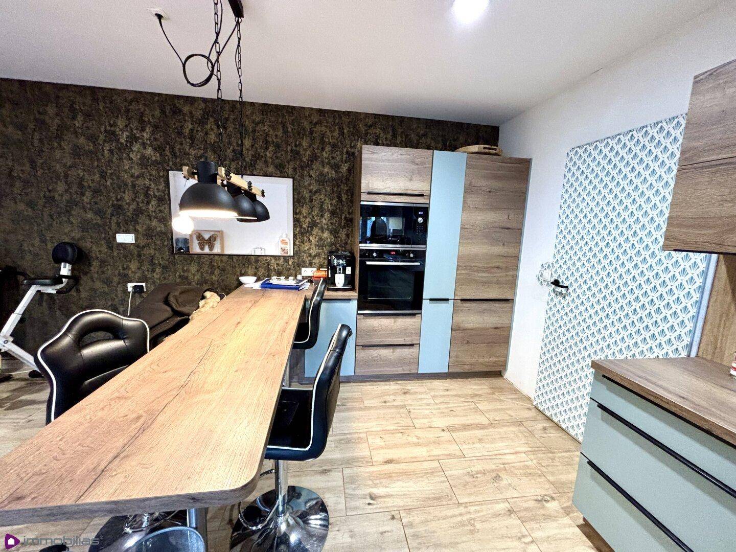 Essbereich in der Küche mit langem Holztisch, Barhockern und integriertem Backofen.