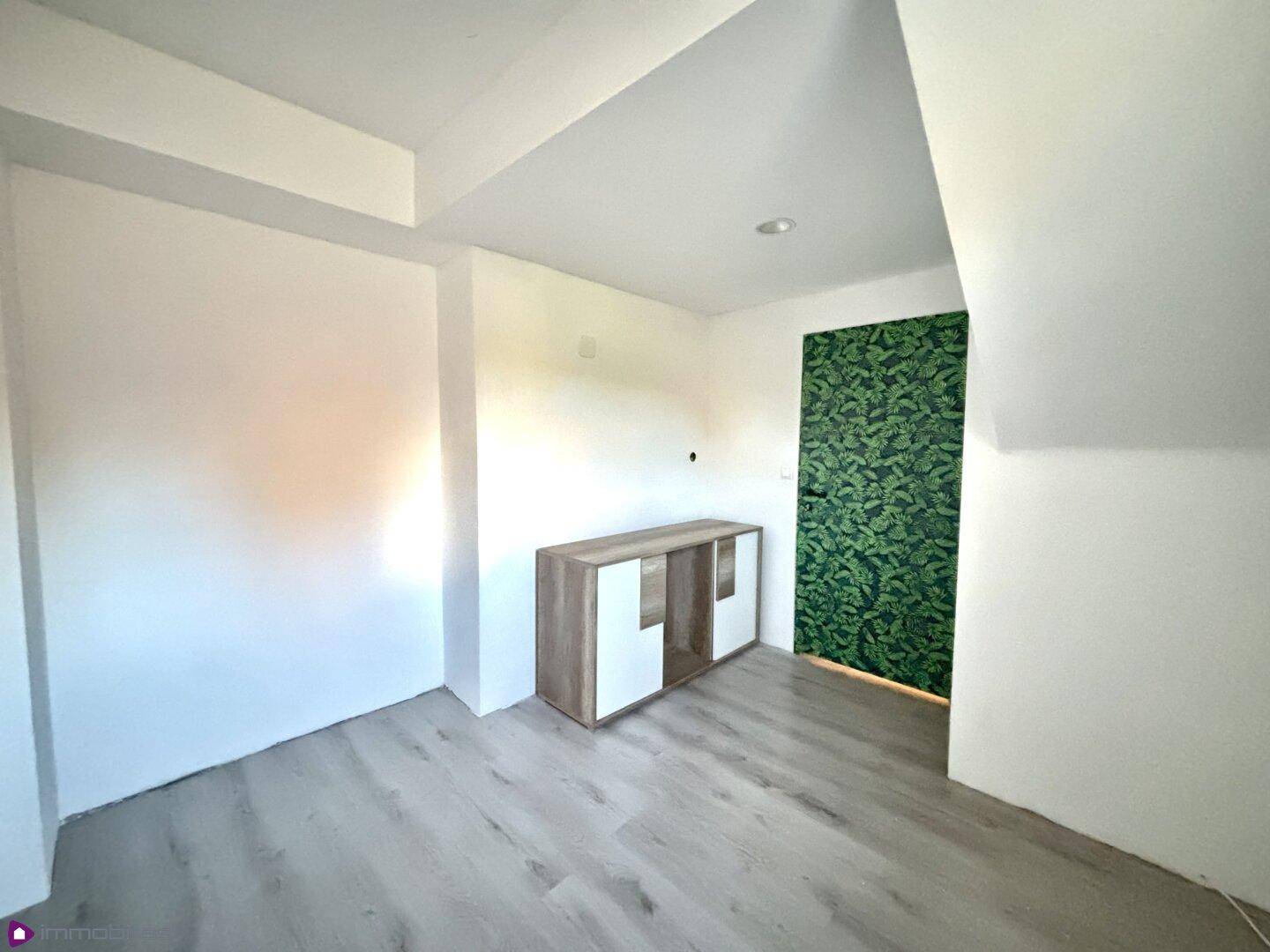 Heller Raum mit Laminatboden und einer auffälligen grünen Mustertapete.