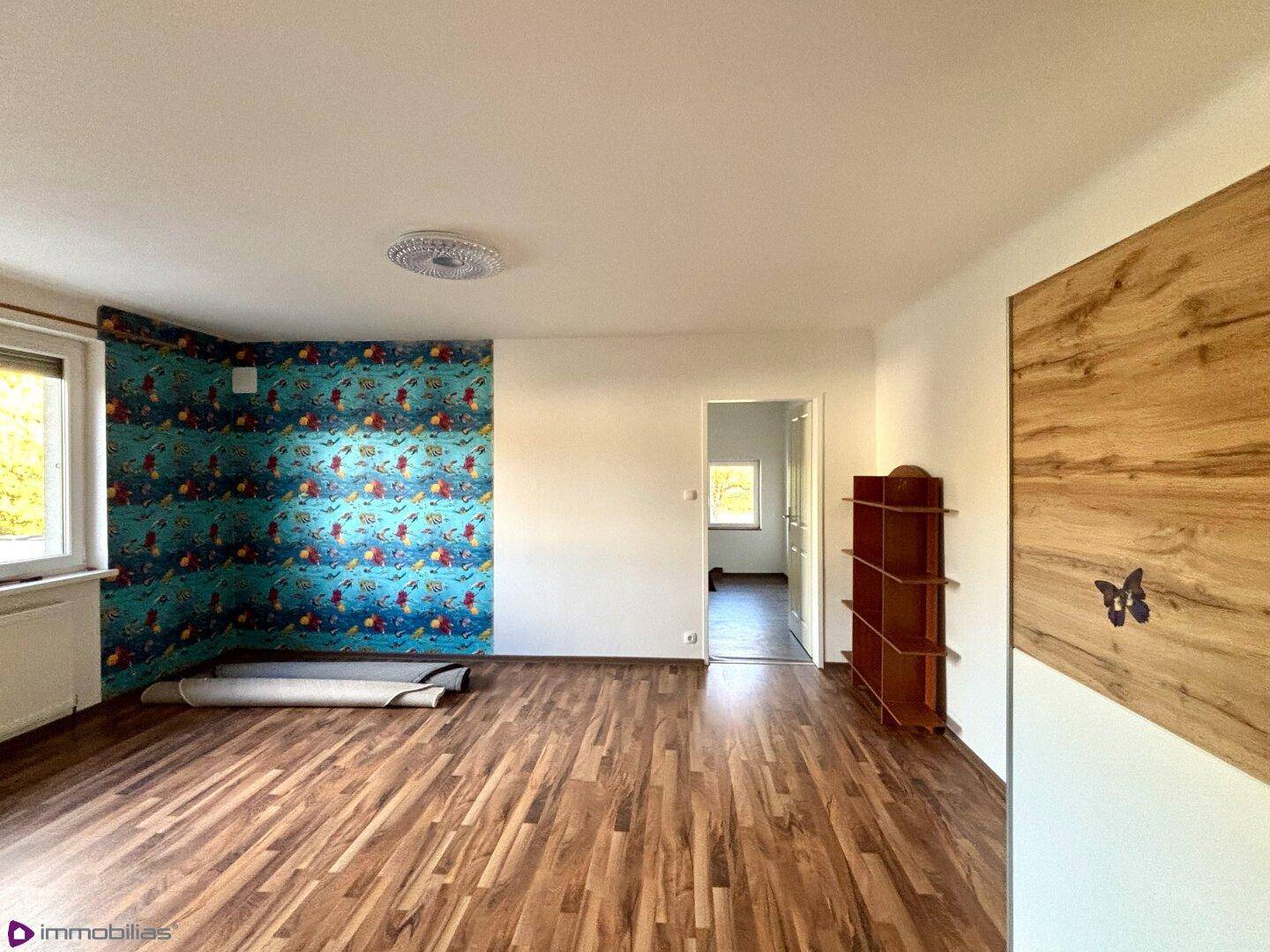 Heller Raum mit Laminatboden, Fenster und bunter Tapete.