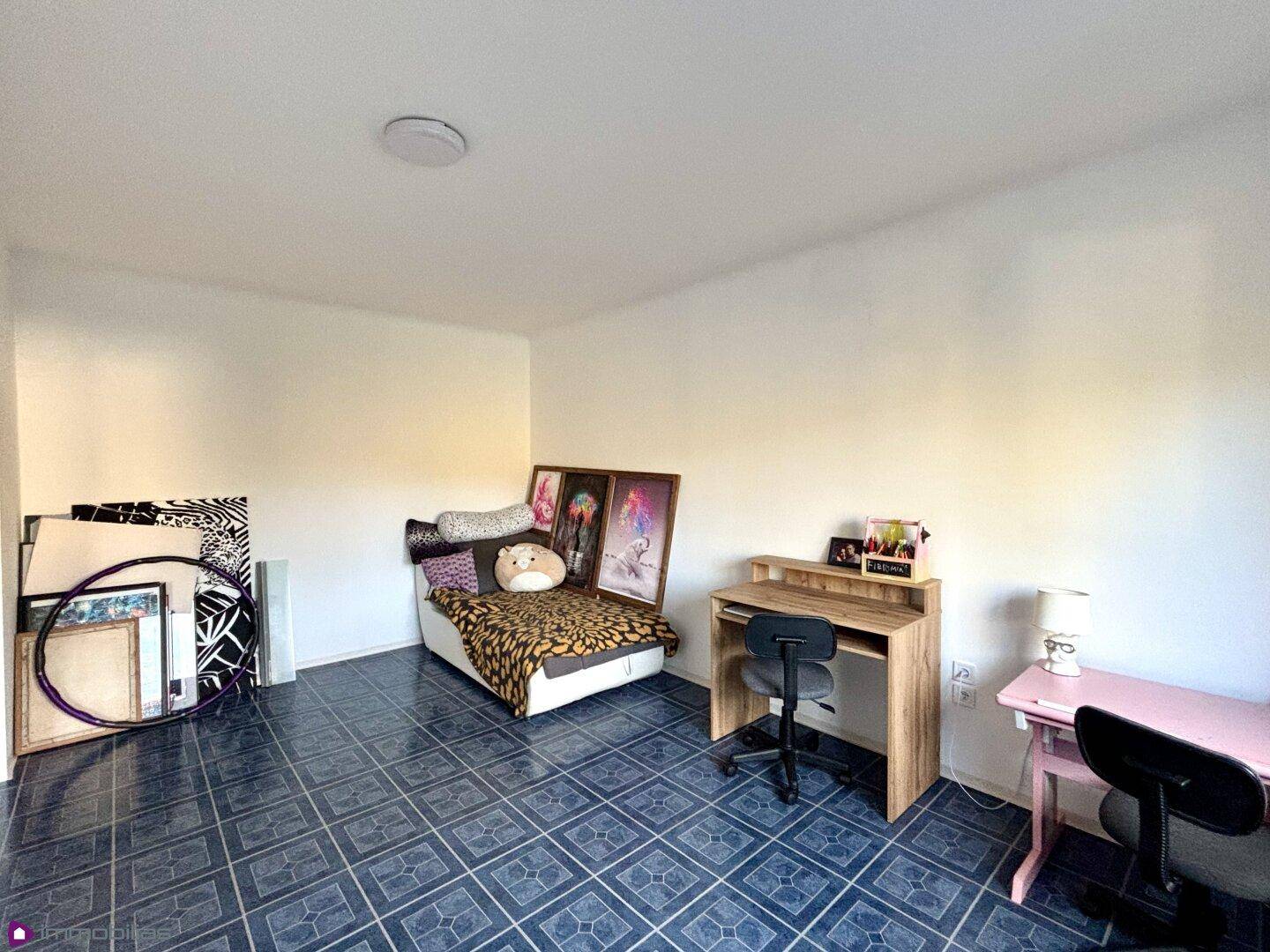 Zimmer mit blauem Fliesenboden, Schreibtisch und Bett.