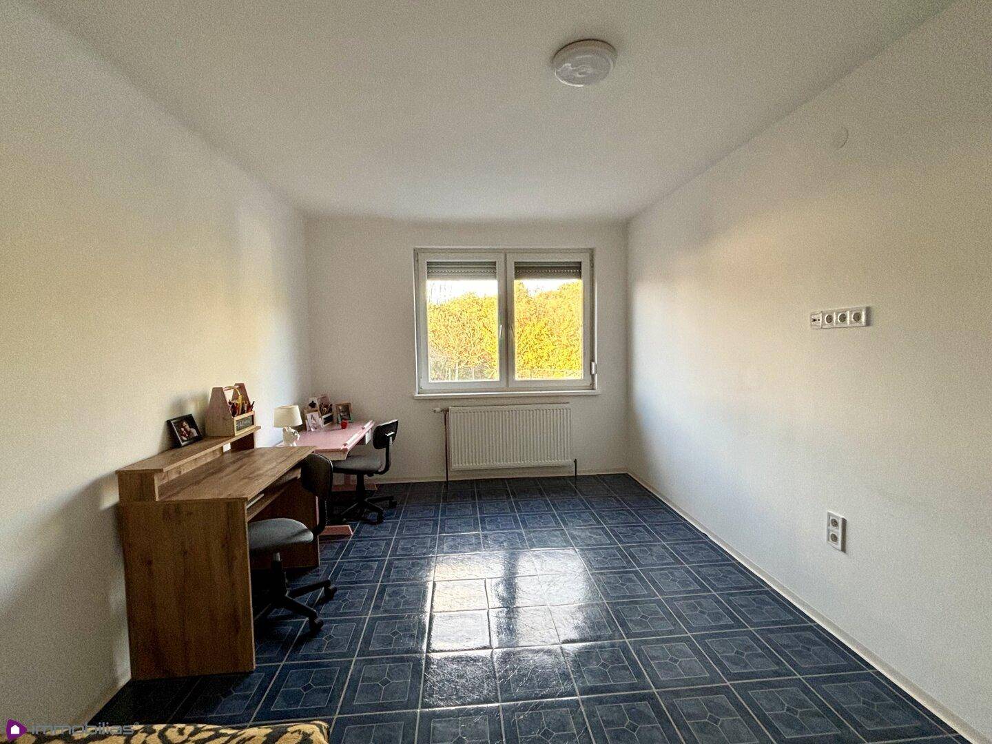 Helles Zimmer mit blauem Fliesenboden, Schreibtisch und Fenster.