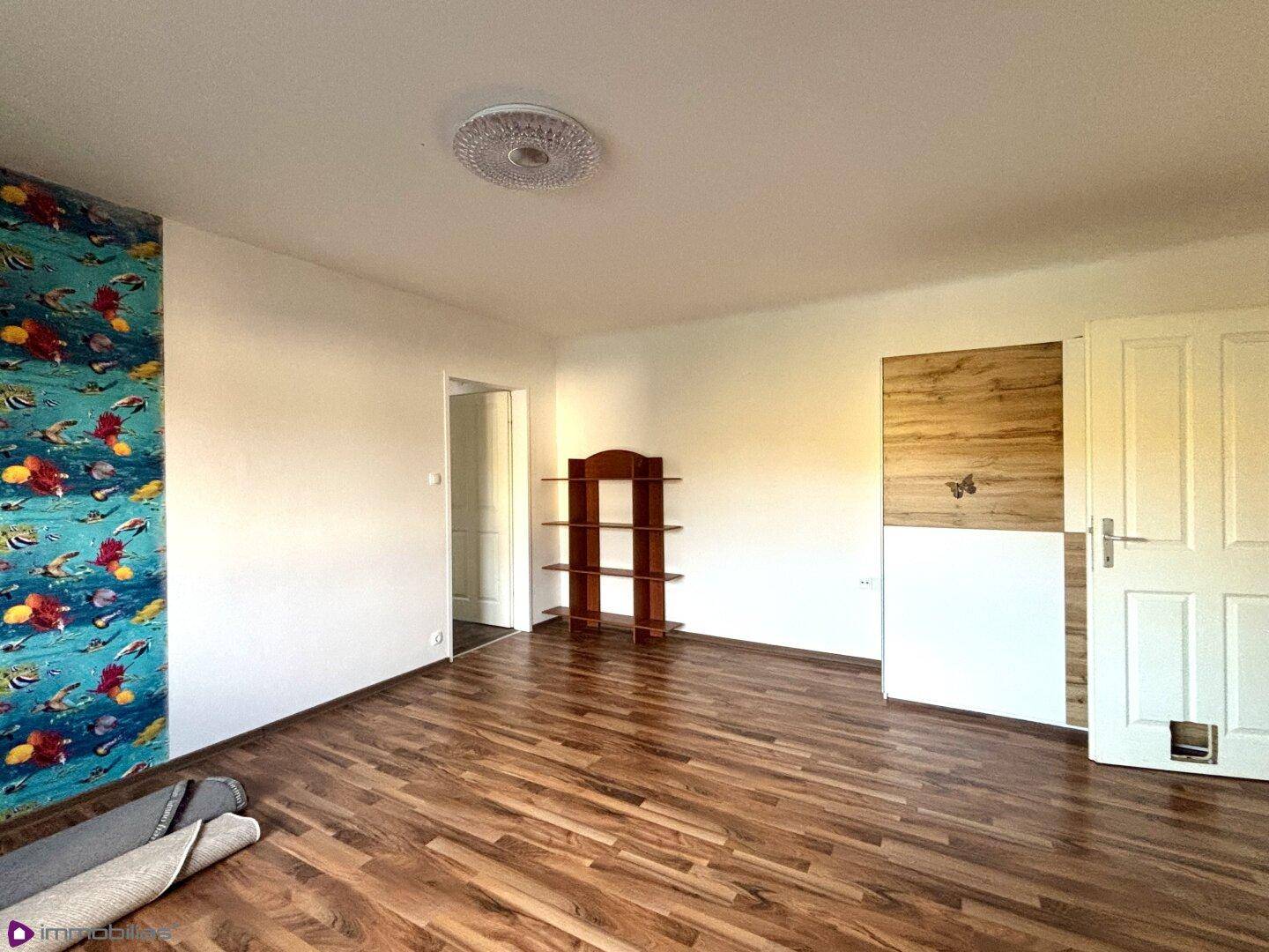 Leerer Raum mit Laminatboden und einer farbenfrohen Mustertapete.