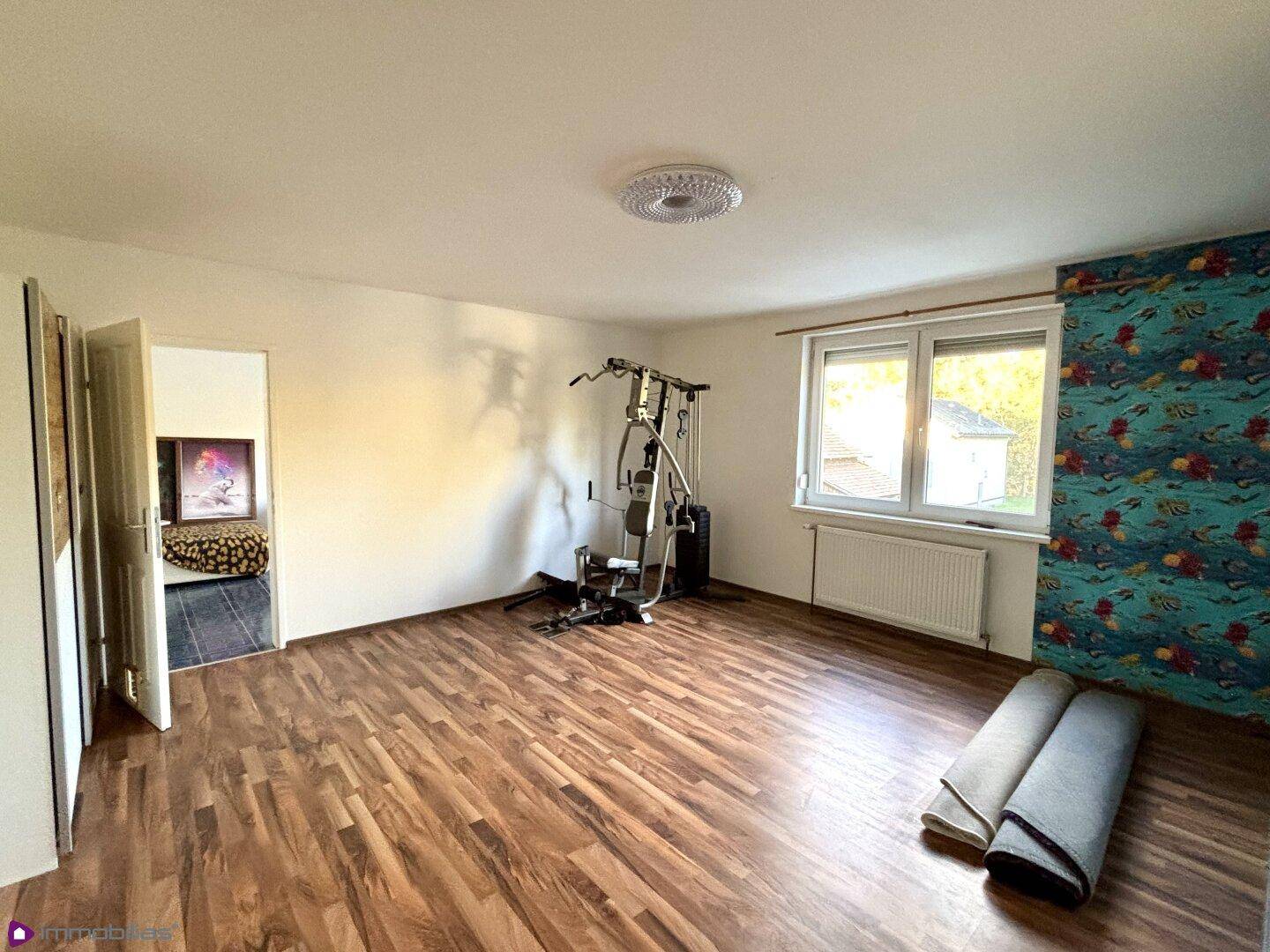 Raum mit Laminatboden, Fenster und Fitnessgeräten.