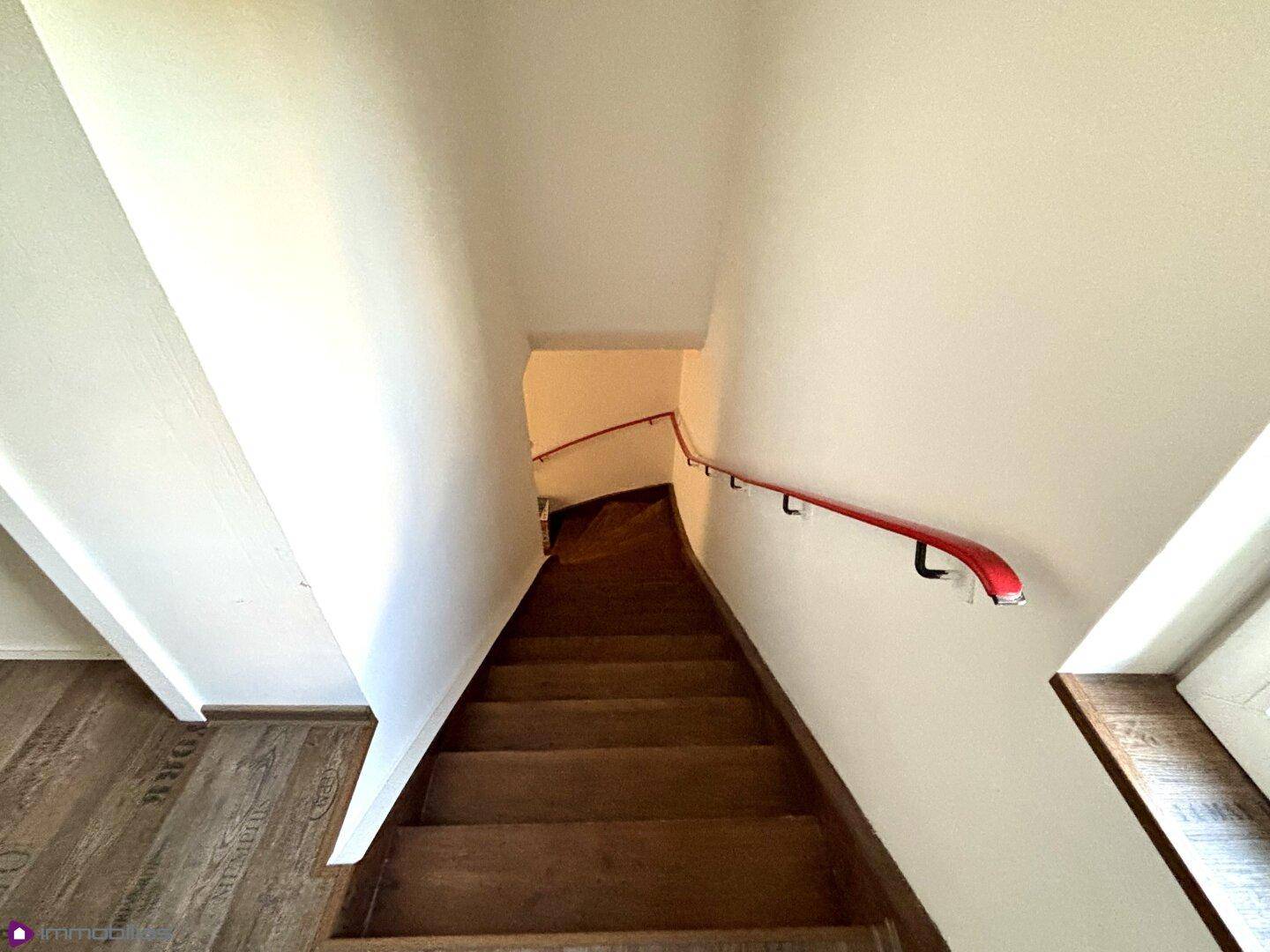 Blick von oben auf die Holztreppe mit rotem Handlauf.